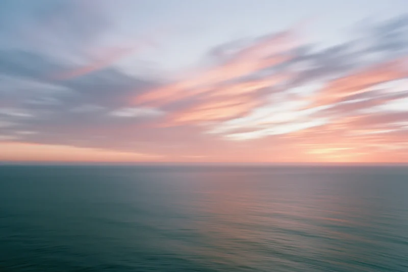 Ocean meeting sky at sunset with soft pastel clouds and calm water surface