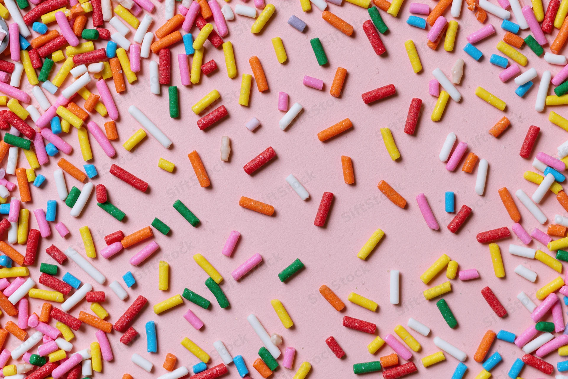 Colorful sprinkles scattered across a pink surface in a flat lay arrangement
