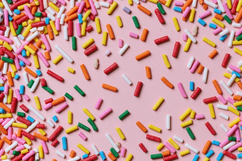Colorful sprinkles scattered across a pink surface in a flat lay arrangement