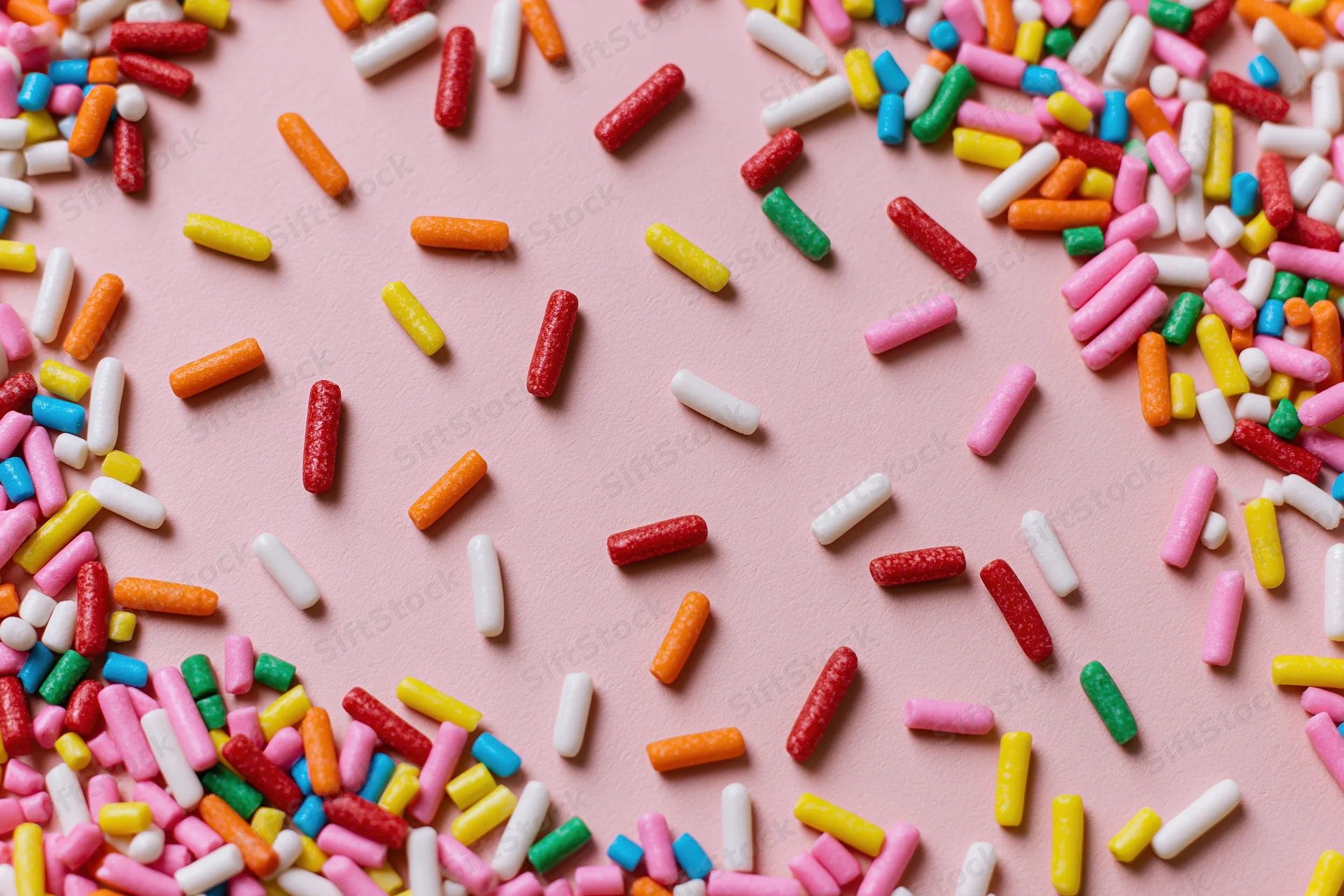 Colorful sprinkles scattered on a pink surface with copyspace in the center