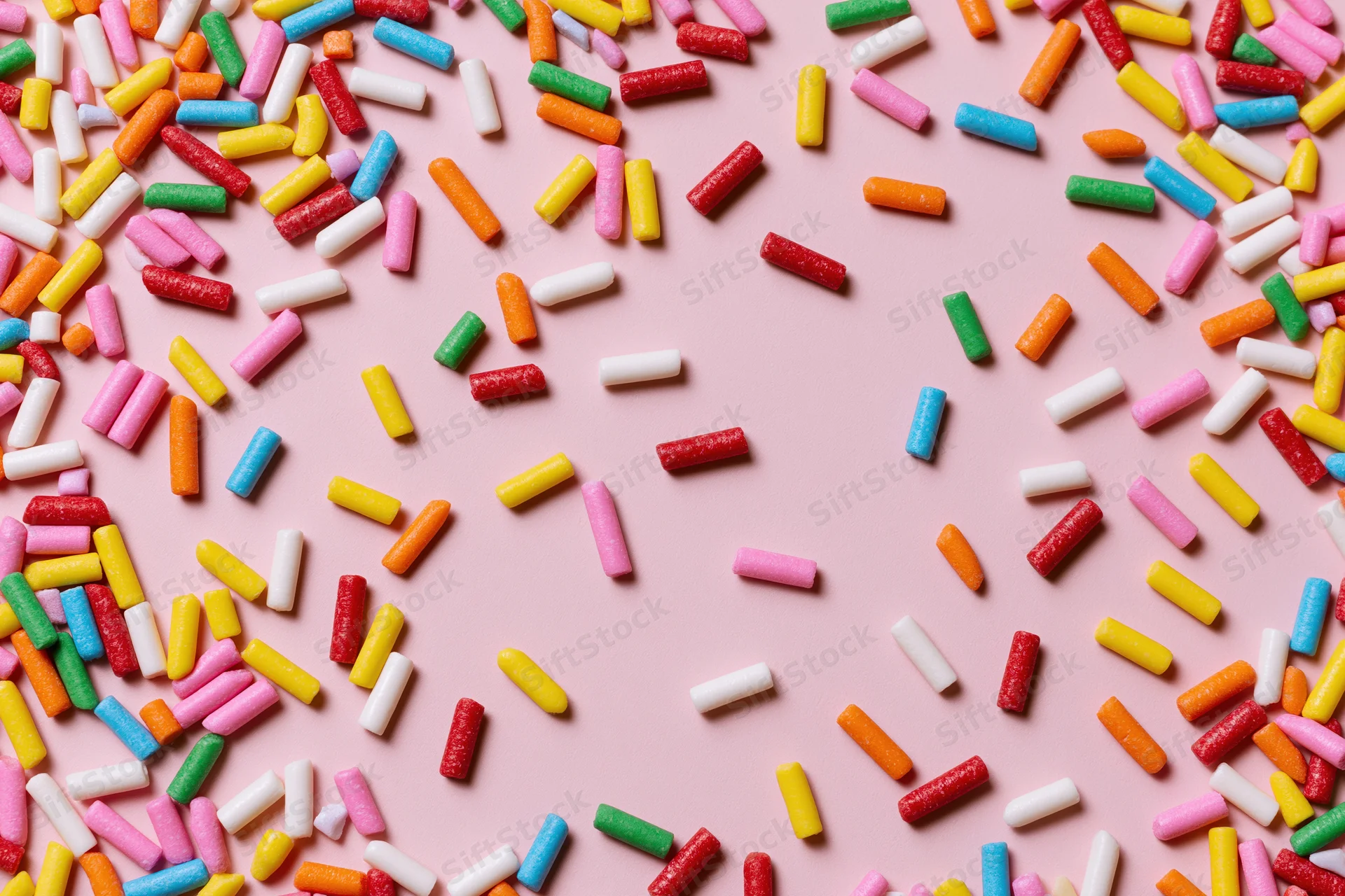 Colorful sprinkles scattered across pink background with copyspace in center