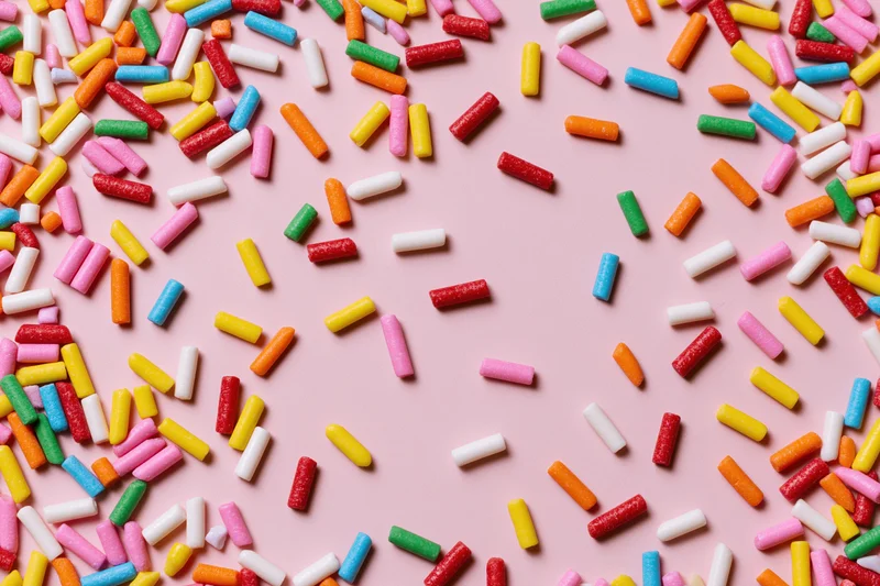 Colorful sprinkles scattered across pink background with copyspace in center