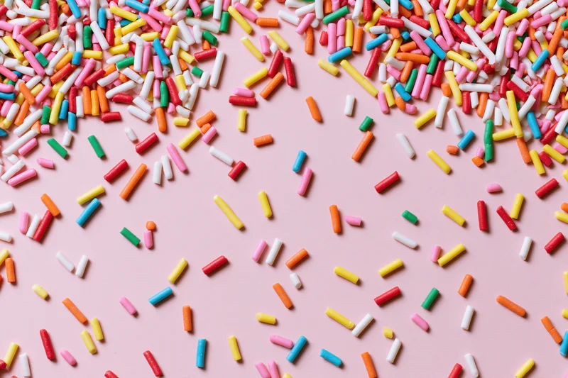 Colorful sprinkles scattered across a pink surface in a flat lay composition