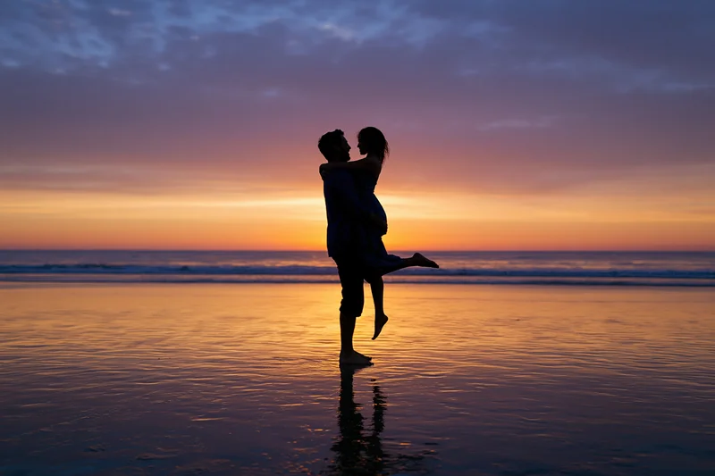 Man lifting woman in embrace on beach at sunset