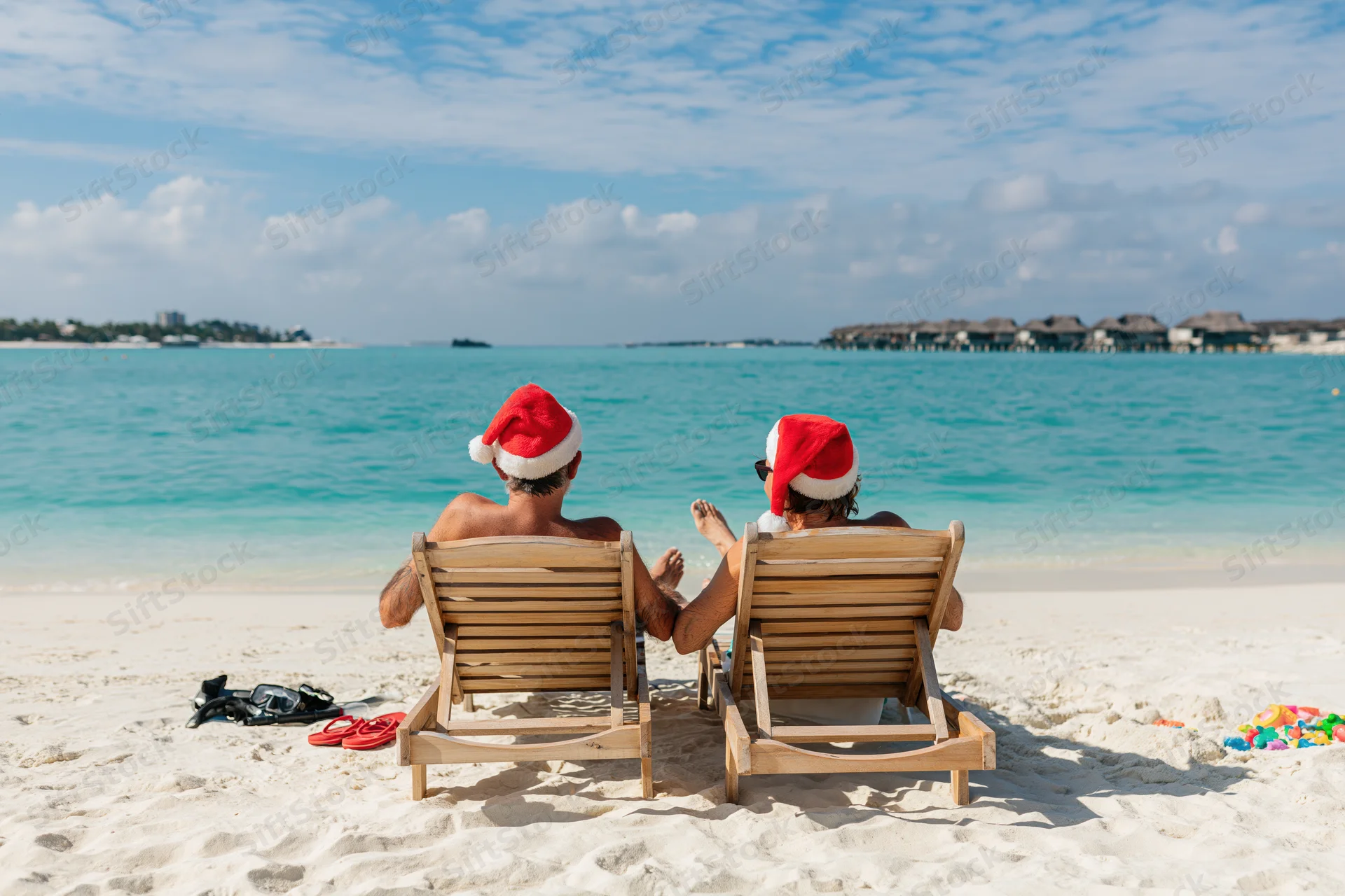 Couple wearing santa hats relaxing on beach chairs by ocean