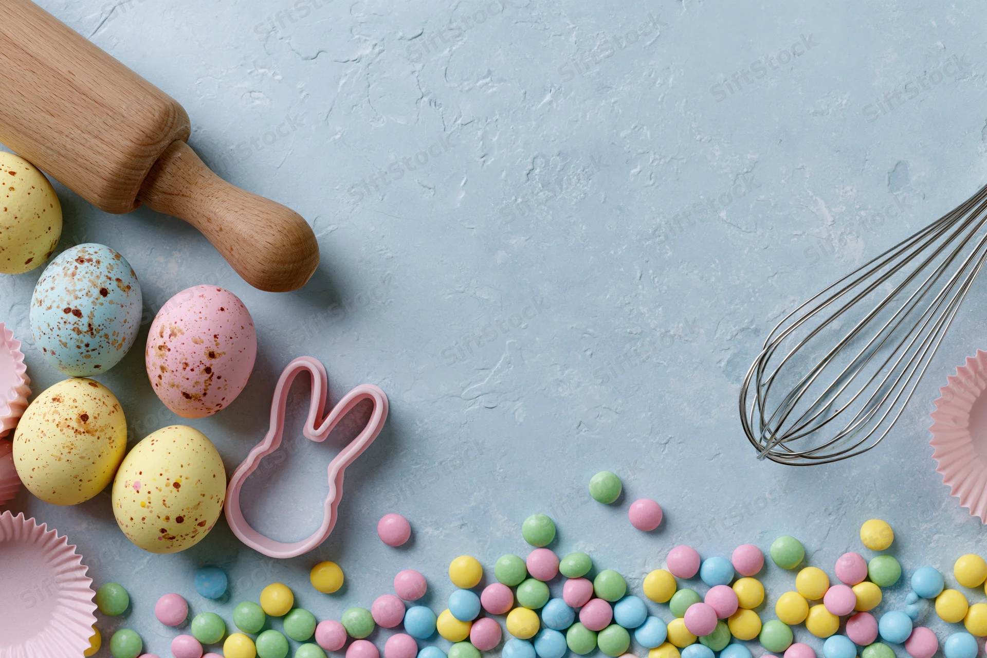 Pastel easter eggs and baking tools arranged on textured blue surface with copyspace