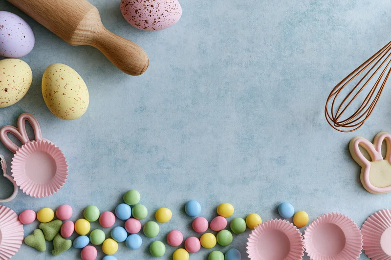 Easter baking setup with pastel eggs, candy, bunny cookies and baking tools on blue surface