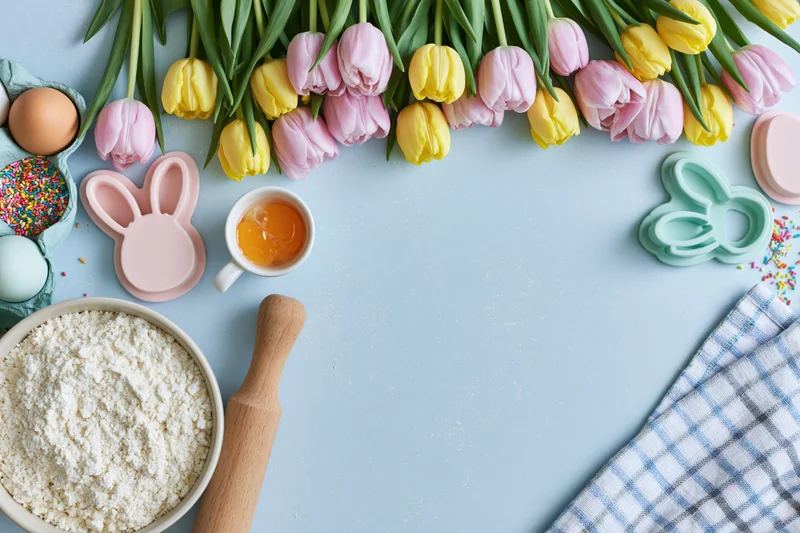 Easter baking setup with tulips and cookie cutters on a pastel blue surface
