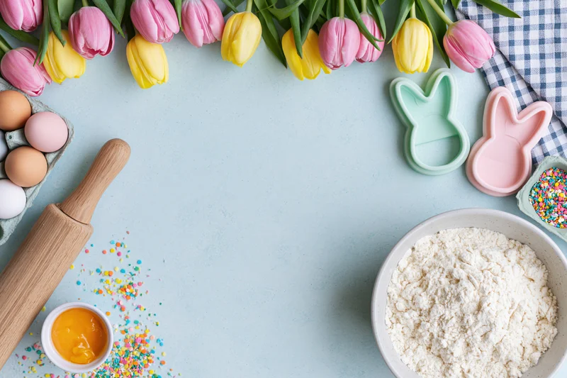 Easter baking ingredients and tulips arranged on a light blue surface with copyspace