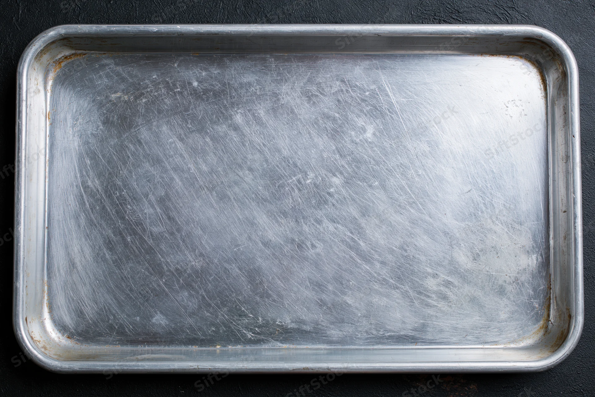 Rectangular metal baking tray with scratched surface on dark background