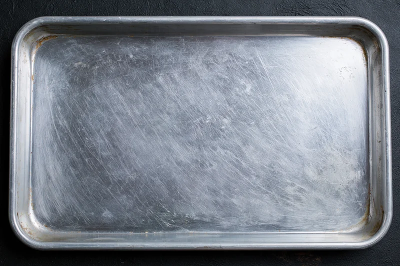 Rectangular metal baking tray with scratched surface on dark background