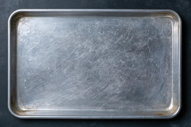 Rectangular metal baking tray with scratches and rust on dark surface, overhead view