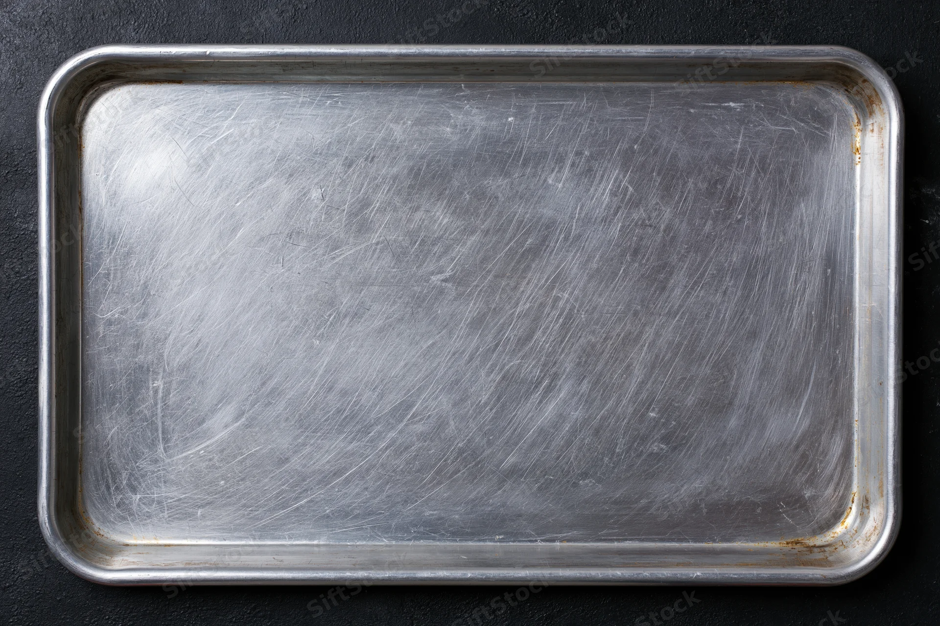 Rectangular metal baking tray with scratched surface on dark background, top view