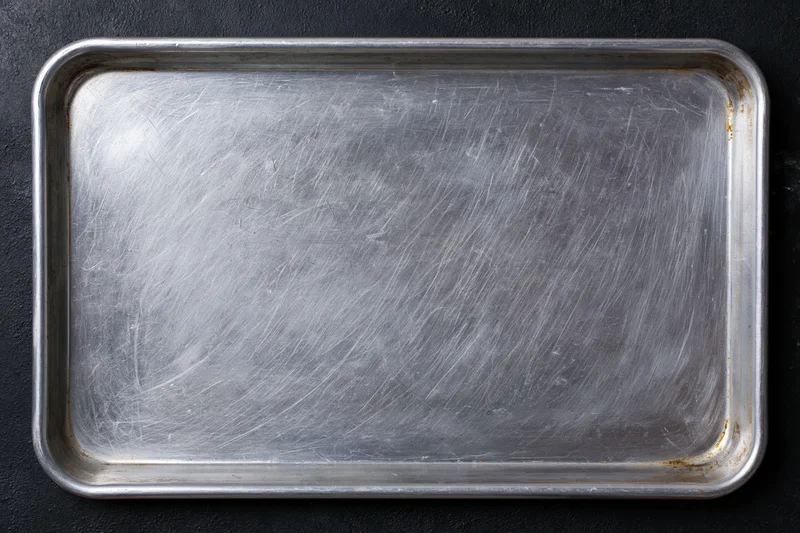 Rectangular metal baking tray with scratched surface on dark background, top view
