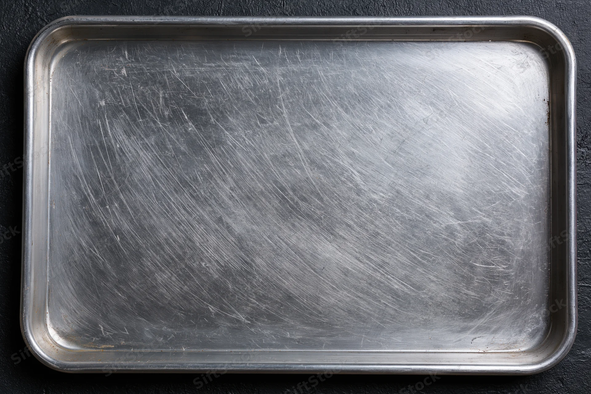 Rectangular metal baking tray with scratched surface on dark background