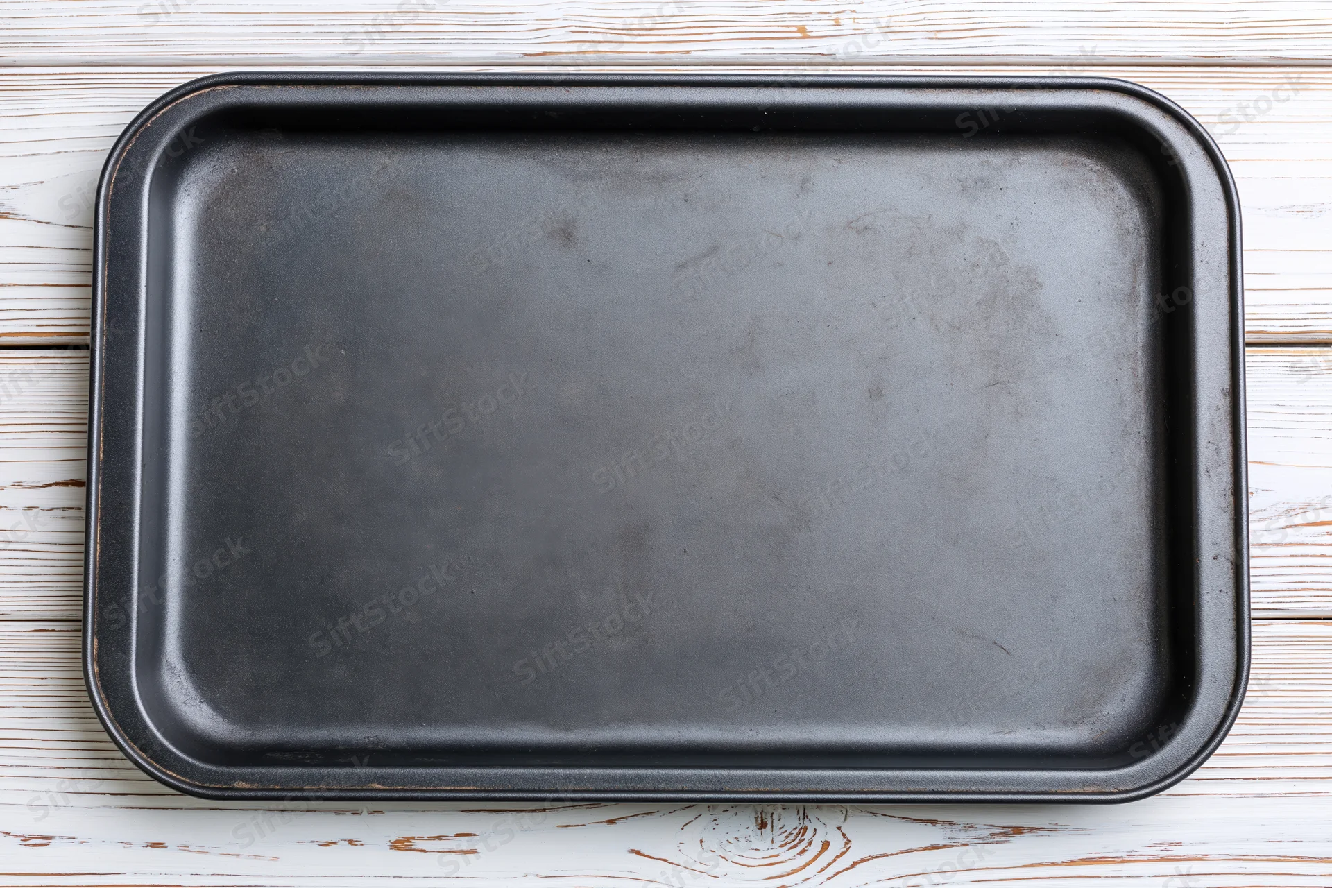 Dark metal baking tray on white wooden surface viewed from above