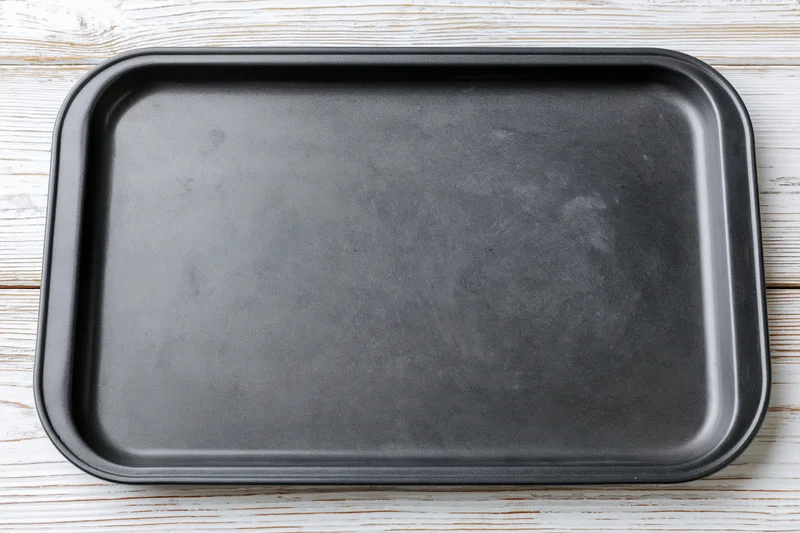 Dark nonstick baking tray on whitewashed wooden surface viewed from above
