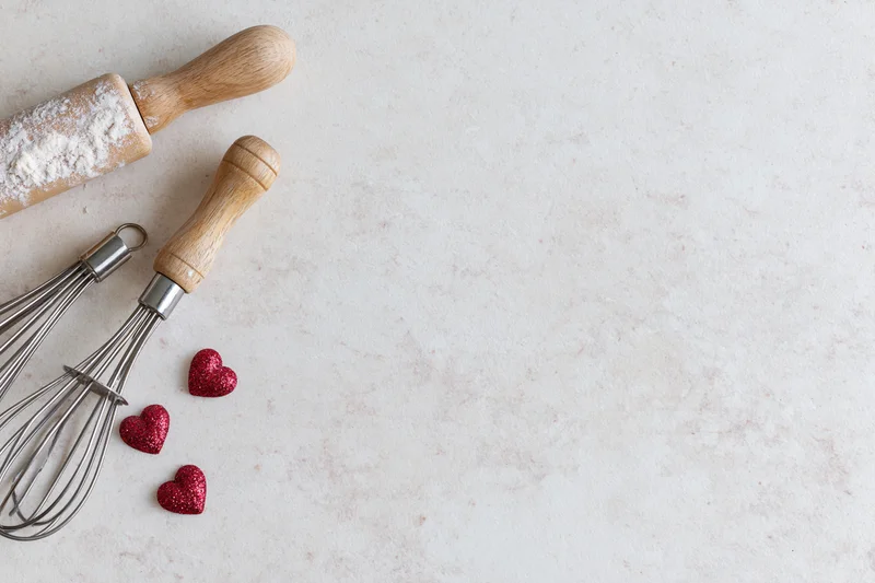 Baking utensils and red glitter hearts arranged on a light marble countertop with copyspace