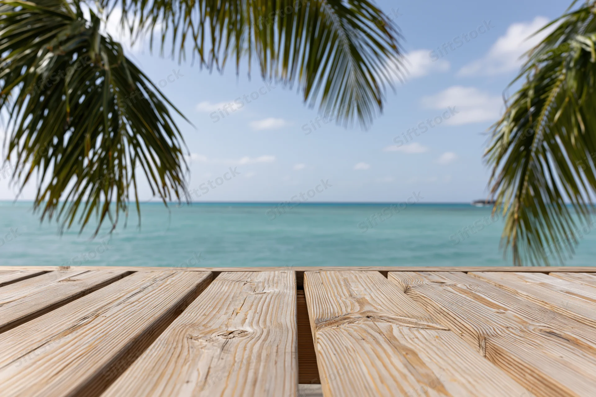 Wooden deck overlooking turquoise ocean under palm fronds at tropical beach