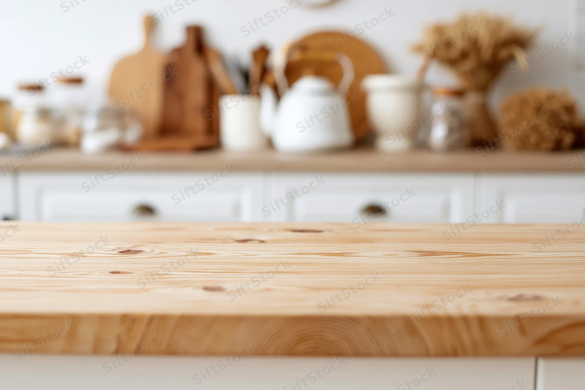 Wooden kitchen countertop in focus with blurred background of white cabinetry and decor