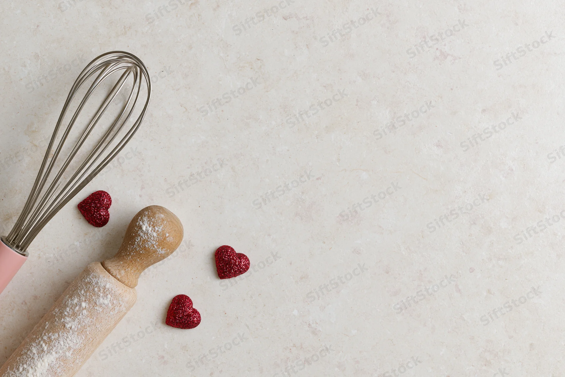 Rolling pin and whisk with flour and red glitter hearts on a countertop for valentine's day baking