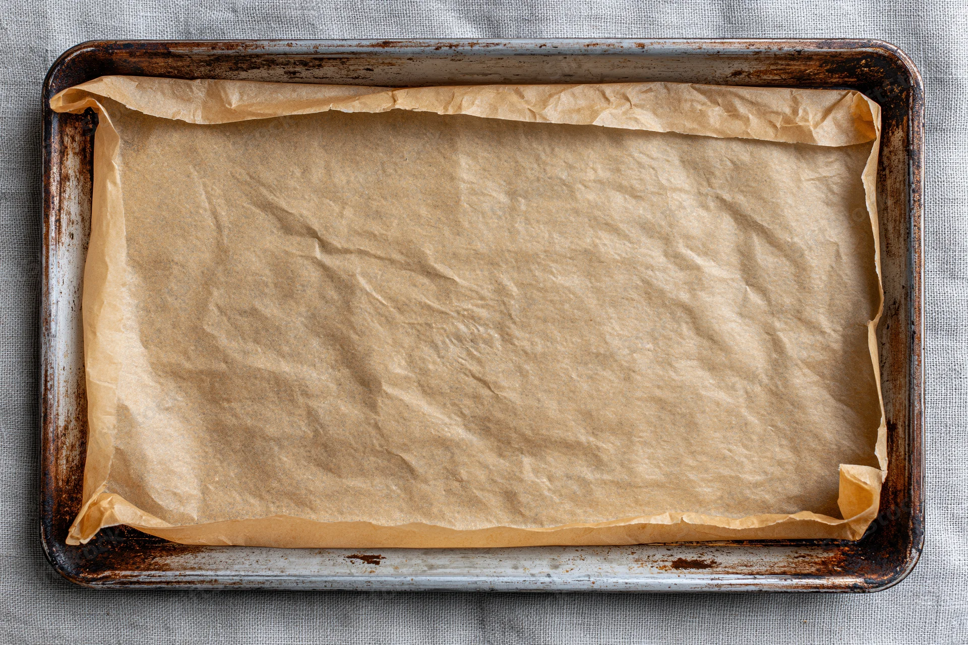 Parchment paper lining a metal baking tray on a gray cloth surface