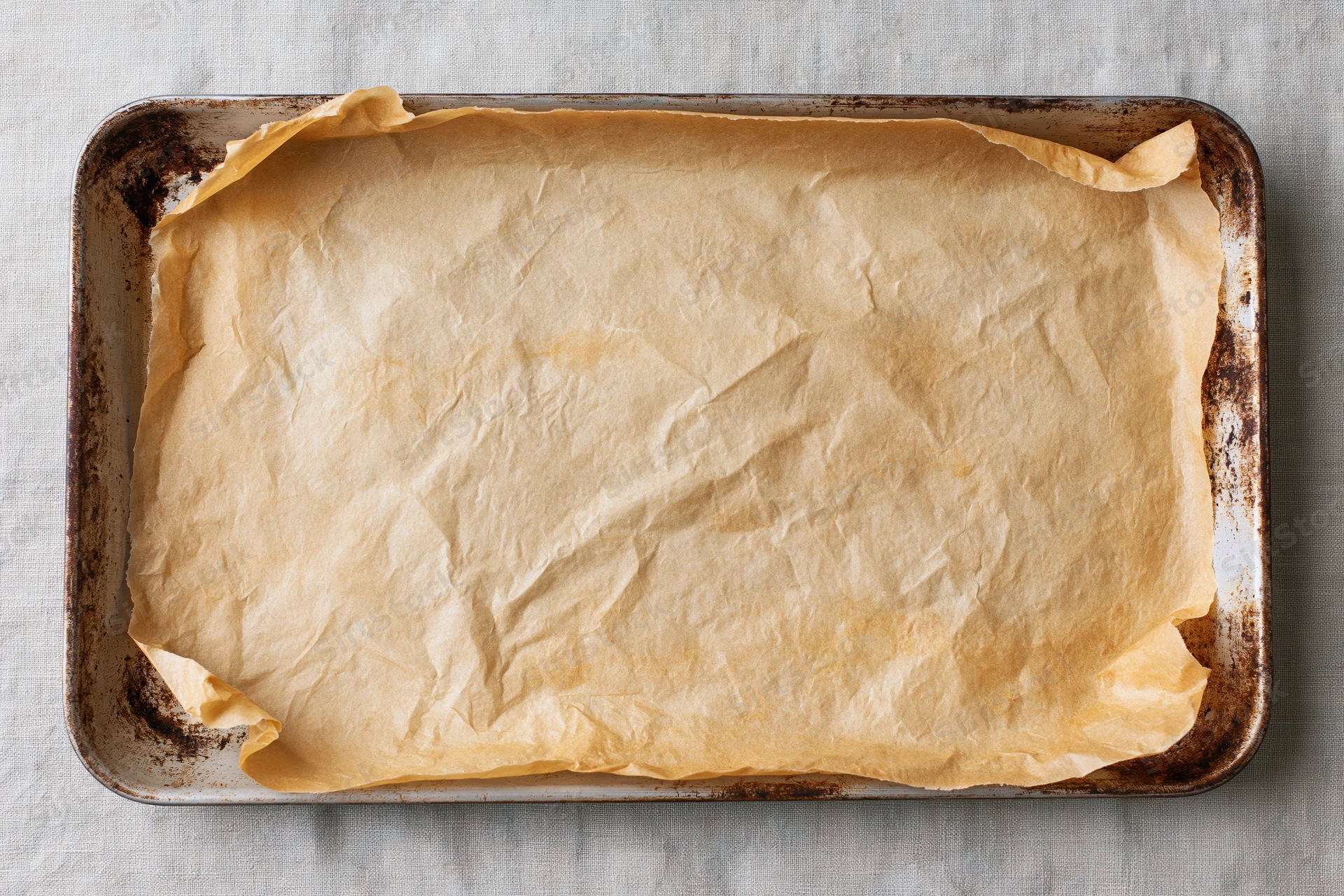Parchment paper lining a metal baking tray on a linen cloth