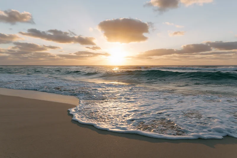 Waves breaking on sandy beach at sunset with clouds in sky