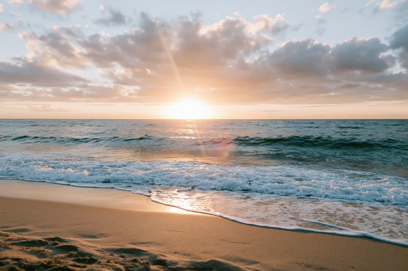 Sunset over ocean waves washing onto sandy beach at golden hour