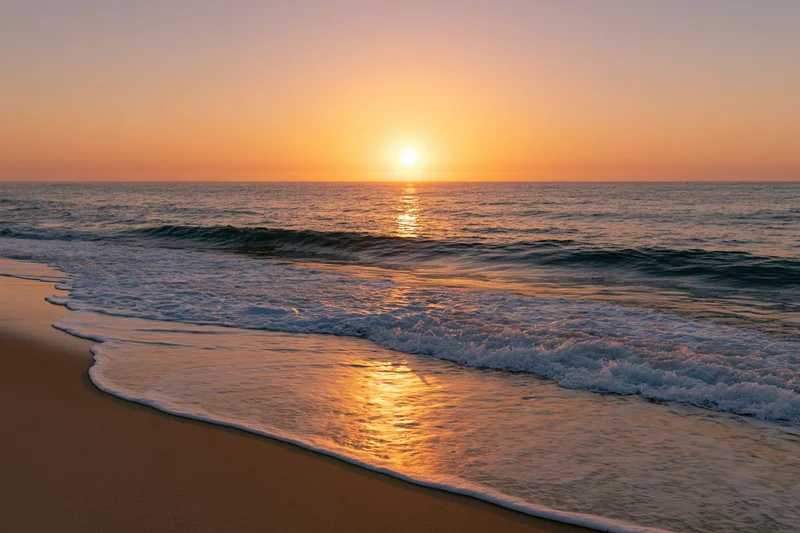 Sunset over ocean with waves rolling onto sandy beach at twilight