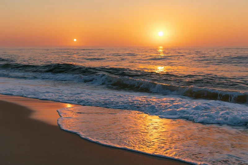 Waves rolling onto sandy beach at sunset with golden light reflecting on water and sand