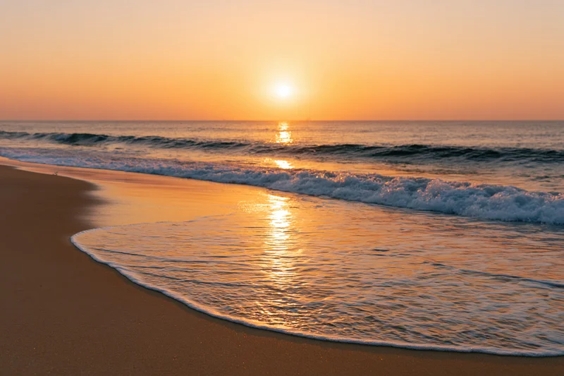 Sunset over ocean waves washing onto sandy beach at twilight