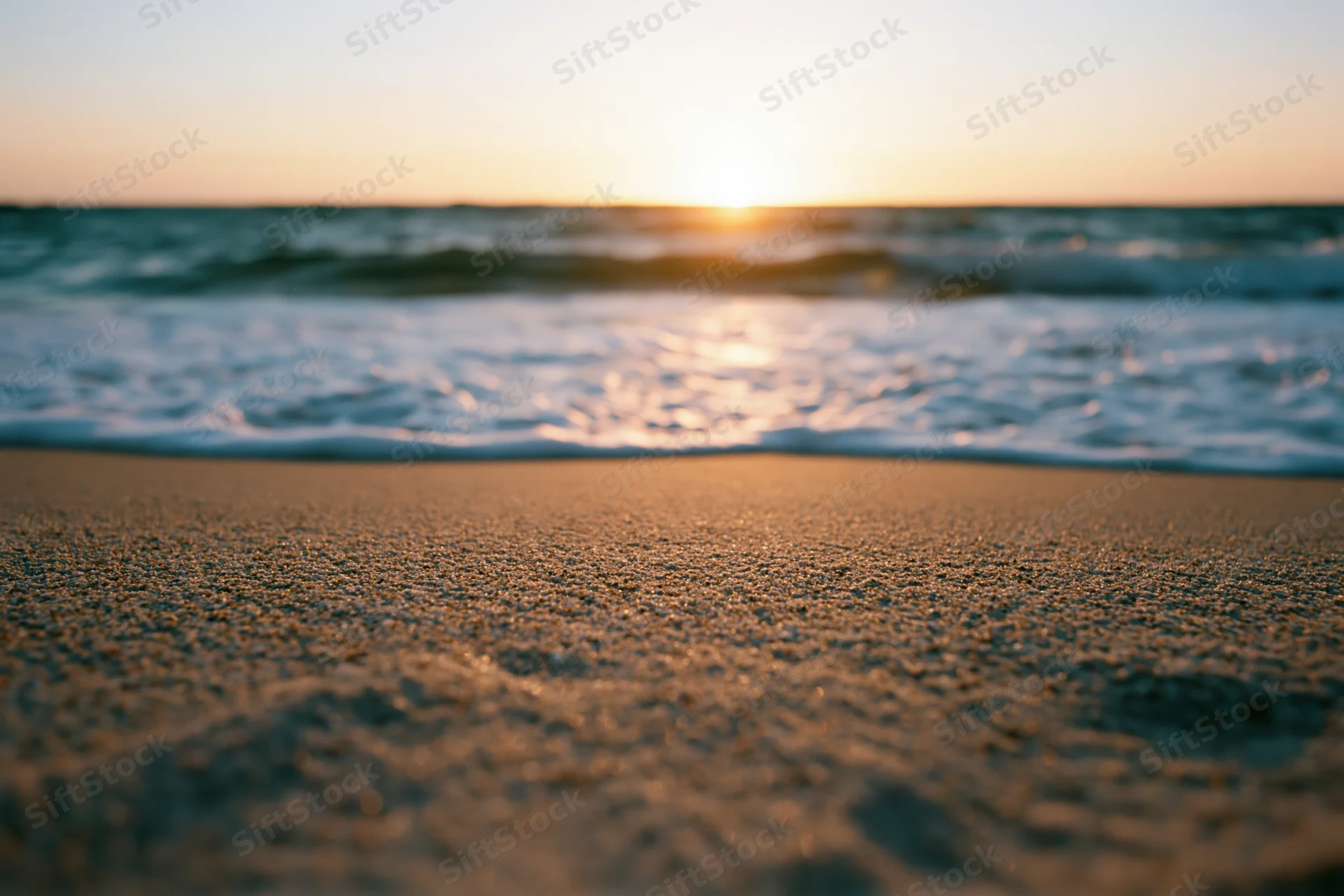 Close-up of wet sand at beach with waves and sunset on horizon