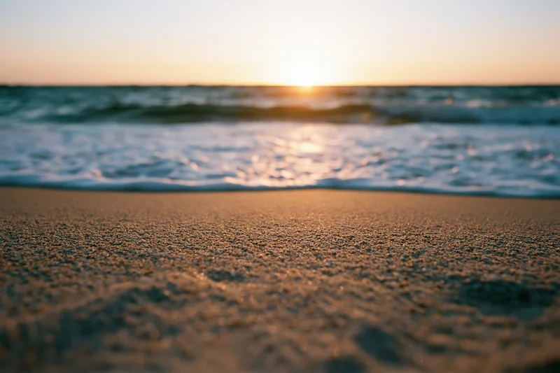 Close-up of wet sand at beach with waves and sunset on horizon
