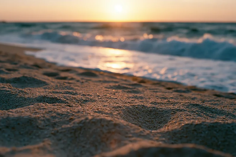 Closeup of wet sand at shoreline with waves and sunset in background