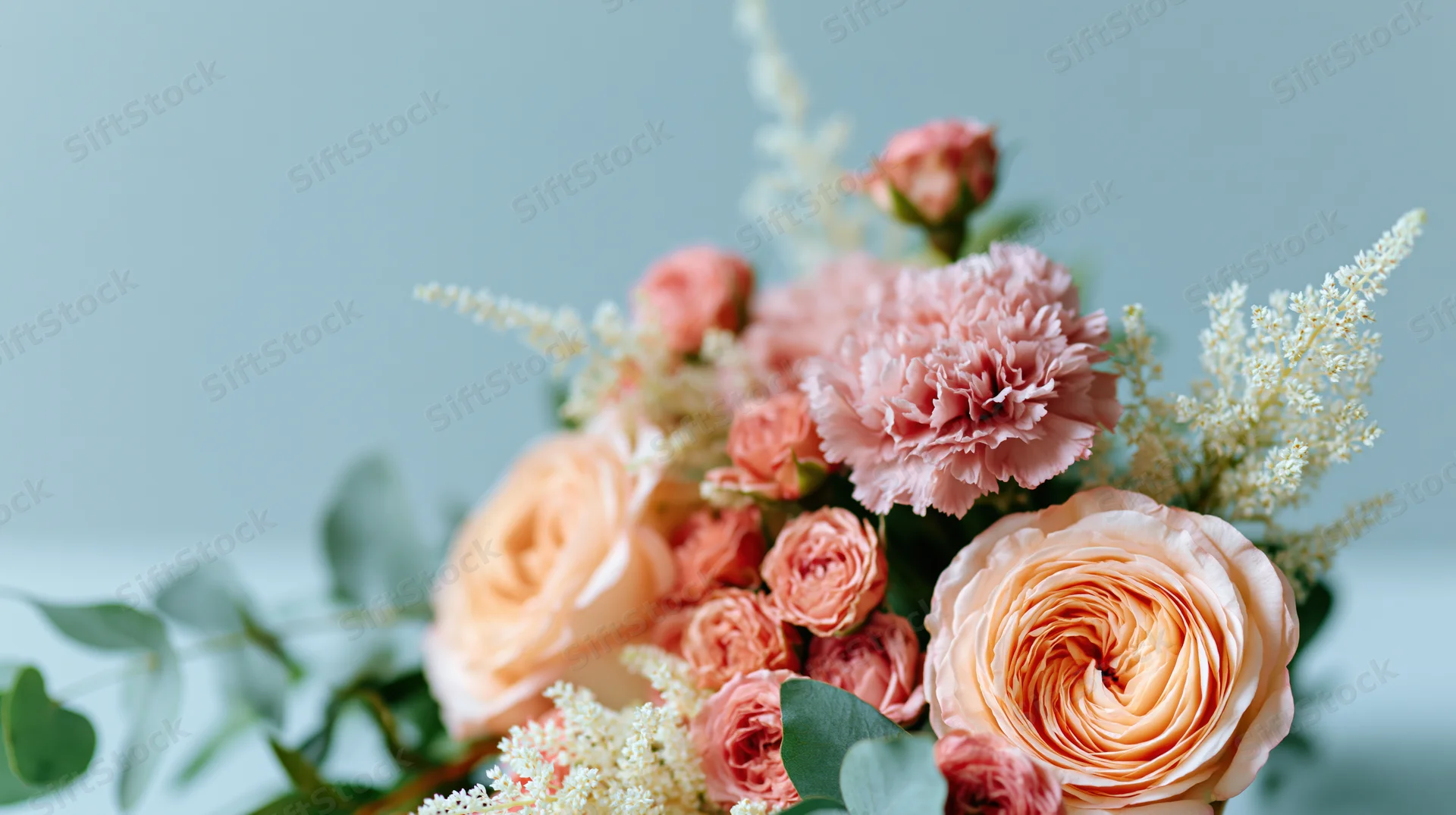 A bouquet of peach roses and pink peonies with astilbe and eucalyptus arranged against a soft blue background
