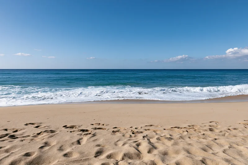 Sandy beach with footprints and waves rolling in under clear blue sky