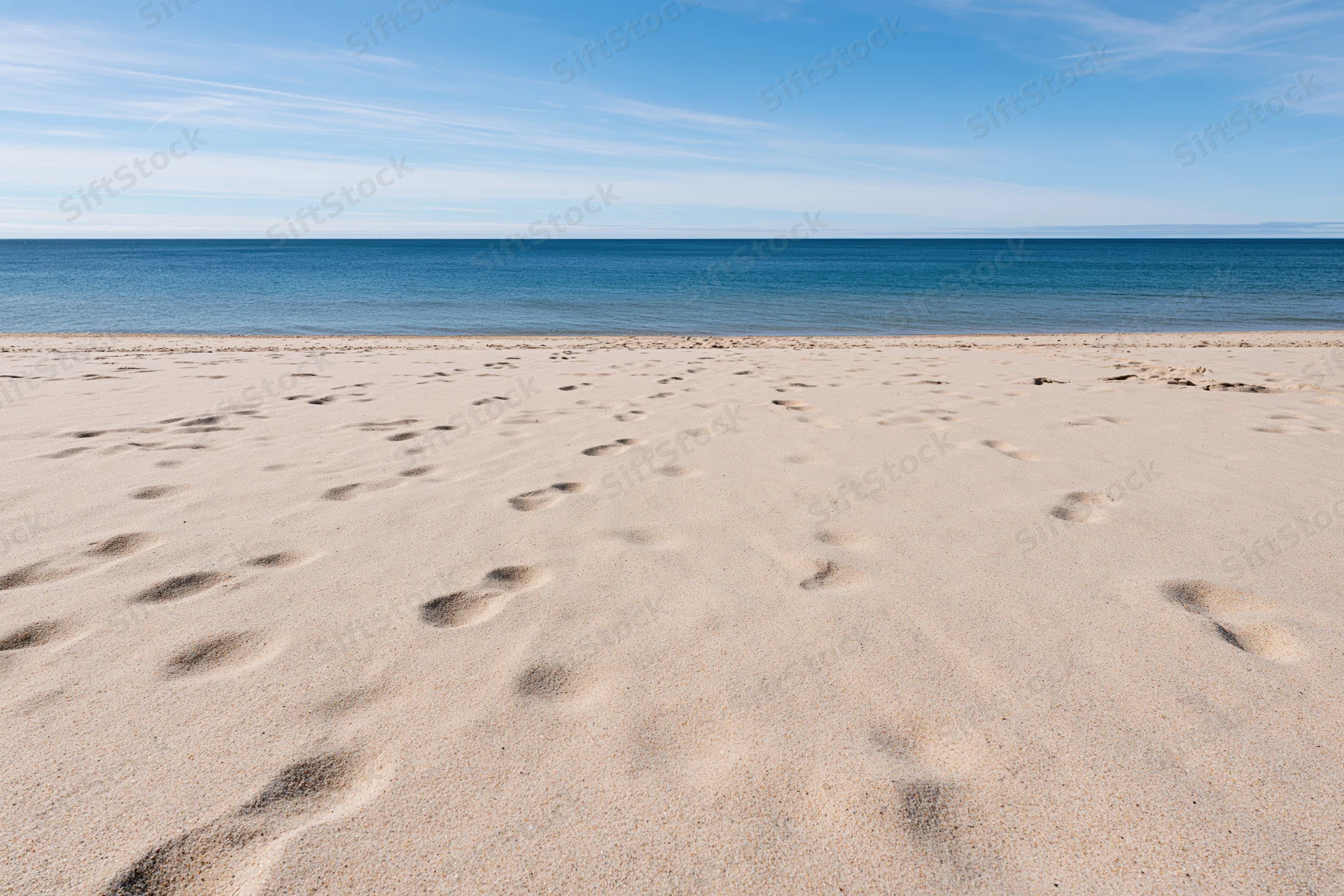 Footprints in the sand along a calm ocean shoreline under a clear blue sky