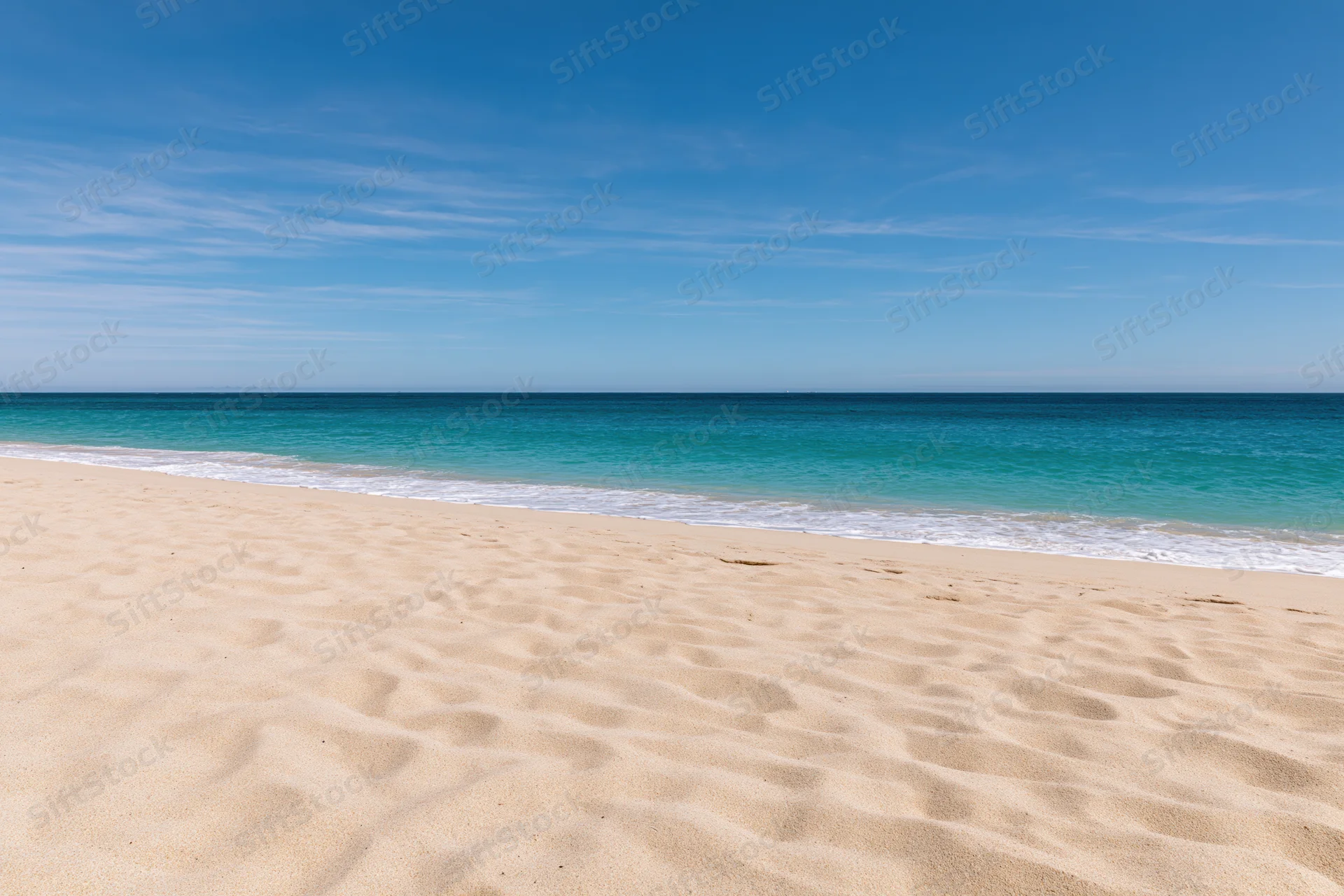 Sandy beach with turquoise ocean waves meeting the shore under a clear blue sky