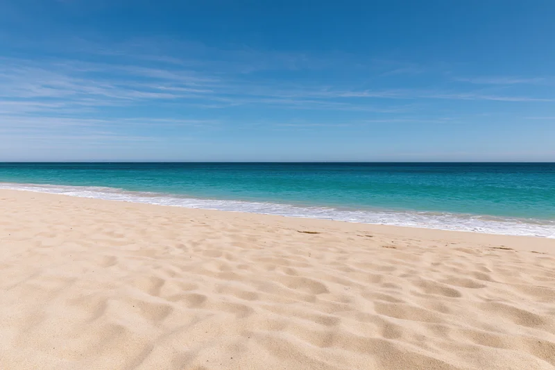 Sandy beach with turquoise ocean waves meeting the shore under a clear blue sky