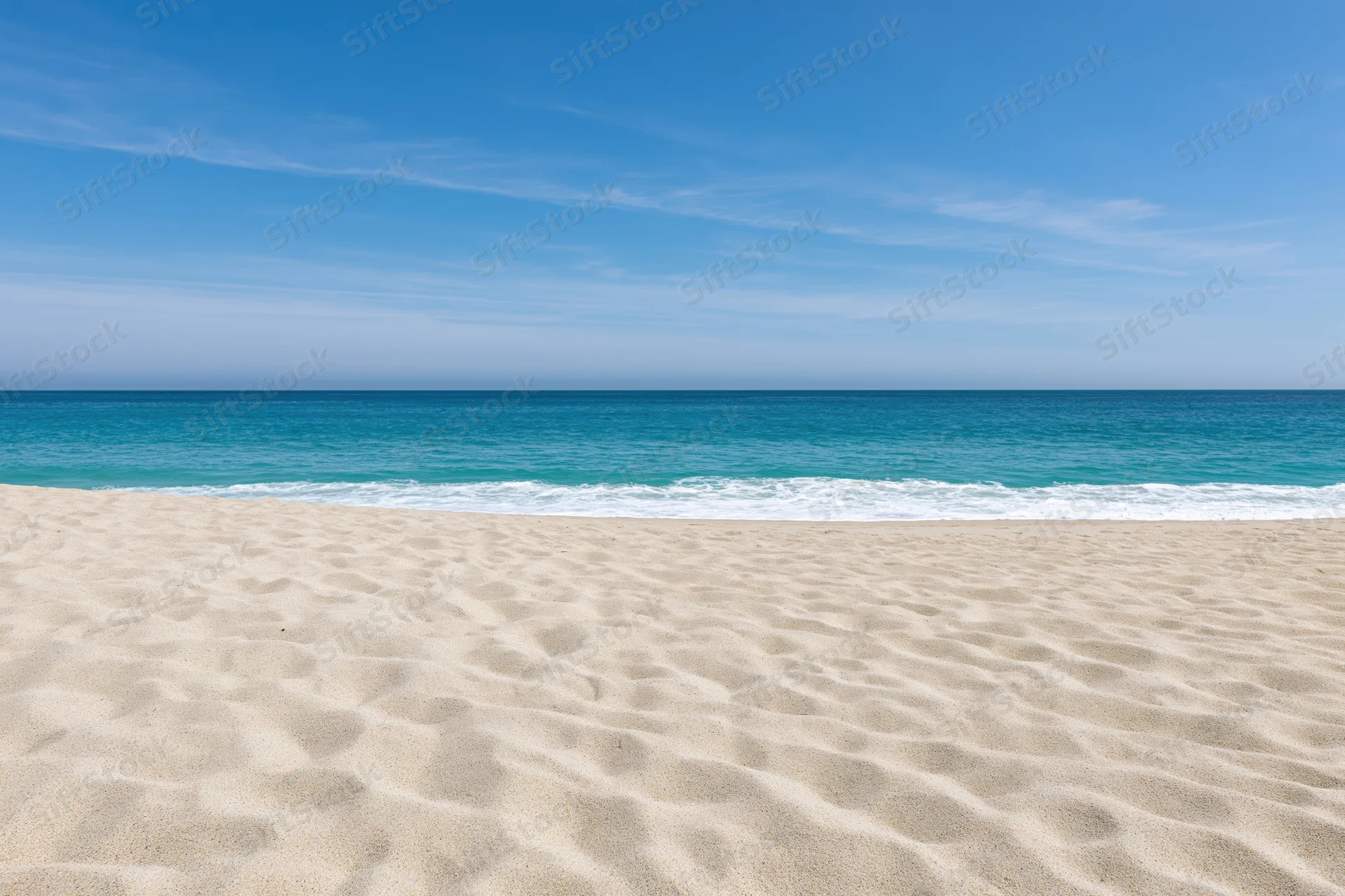 Sandy beach with gentle waves meeting turquoise ocean under clear blue sky