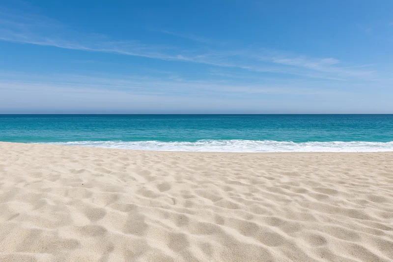 Sandy beach with gentle waves meeting turquoise ocean under clear blue sky