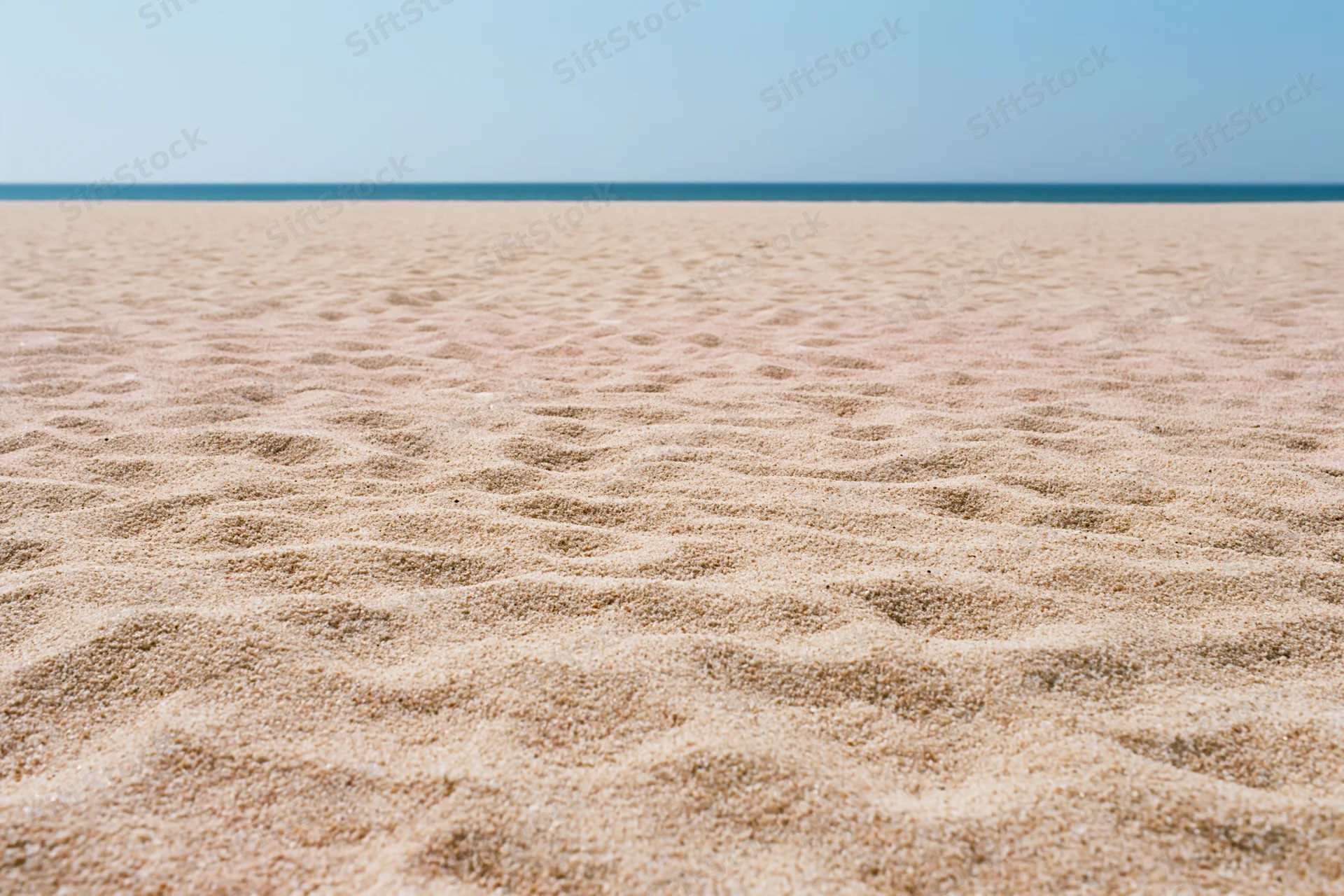 Textured sand on a beach stretching to the ocean horizon under a clear blue sky