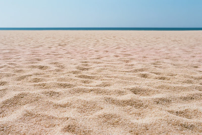 Textured sand on a beach stretching to the ocean horizon under a clear blue sky