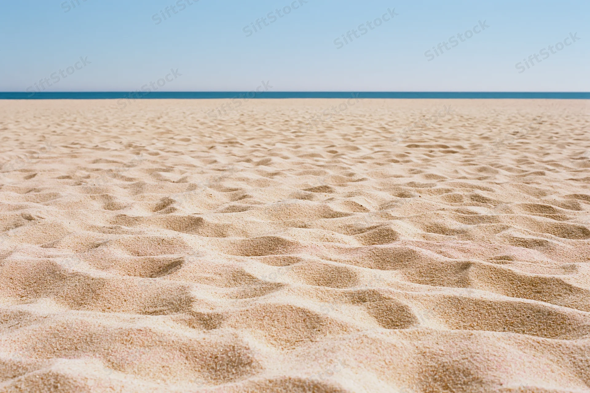 Textured sand on a beach with ocean and sky in the distance