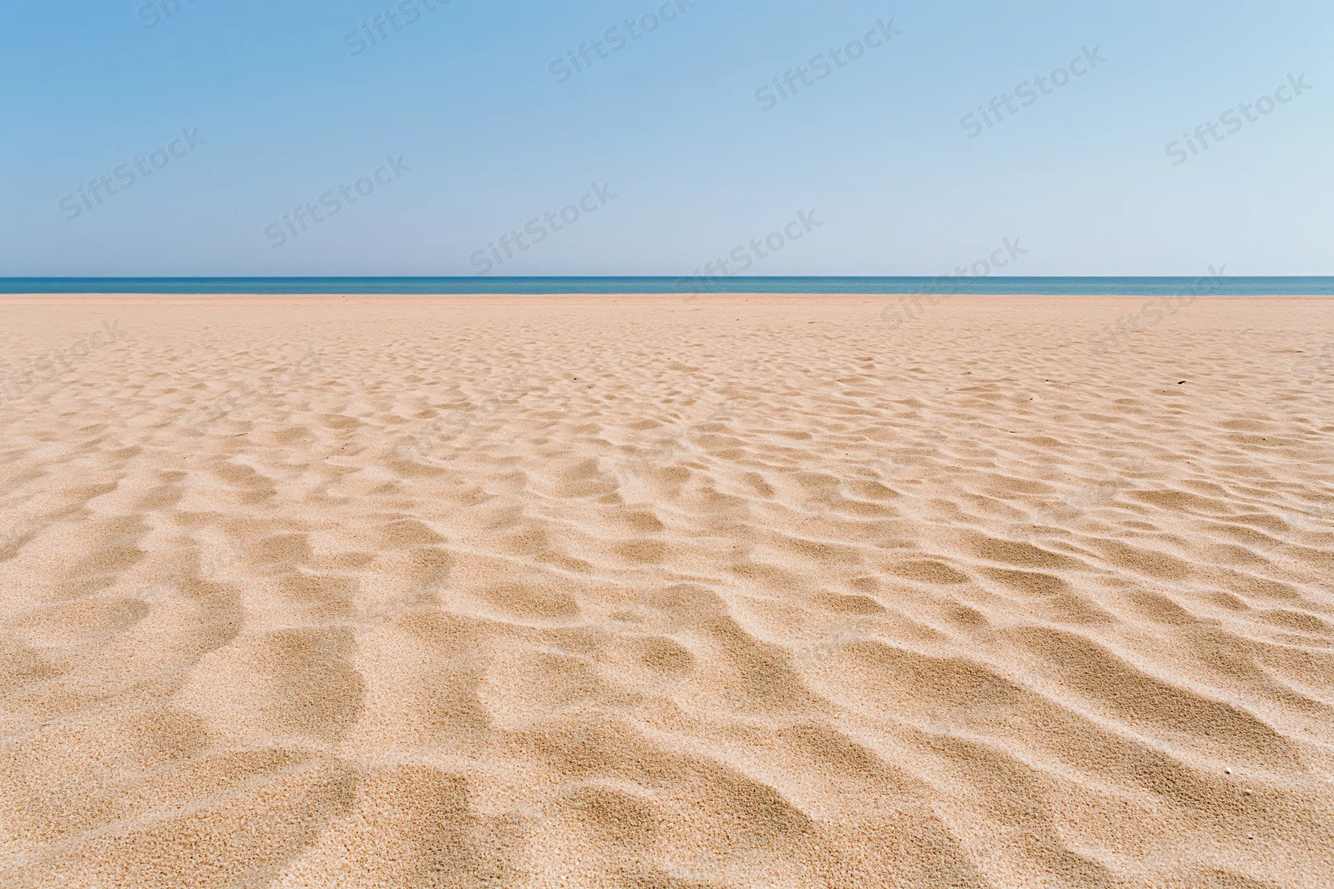 Rippled sand stretching to the ocean under a clear blue sky