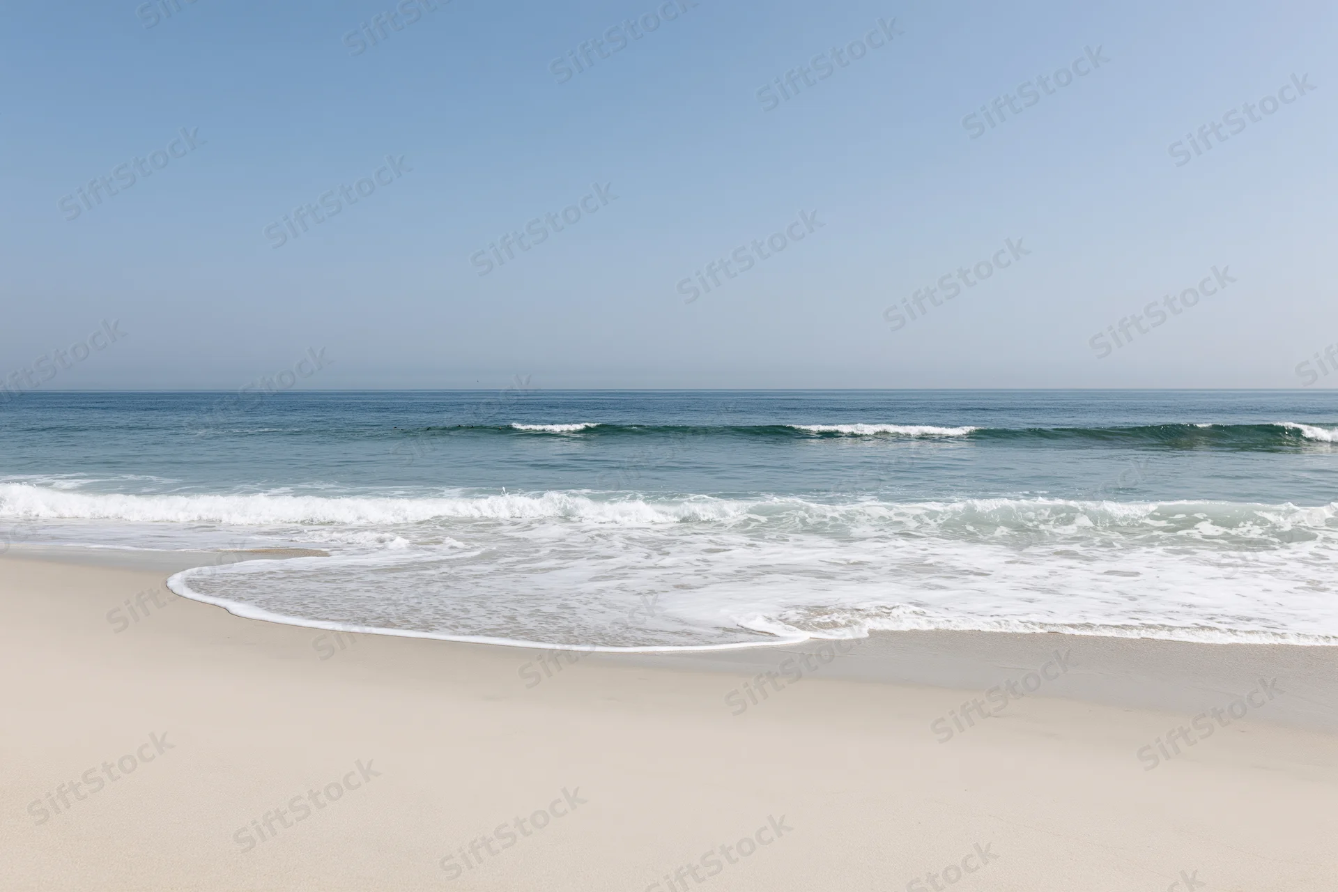 Waves breaking on a sandy beach under a clear blue sky