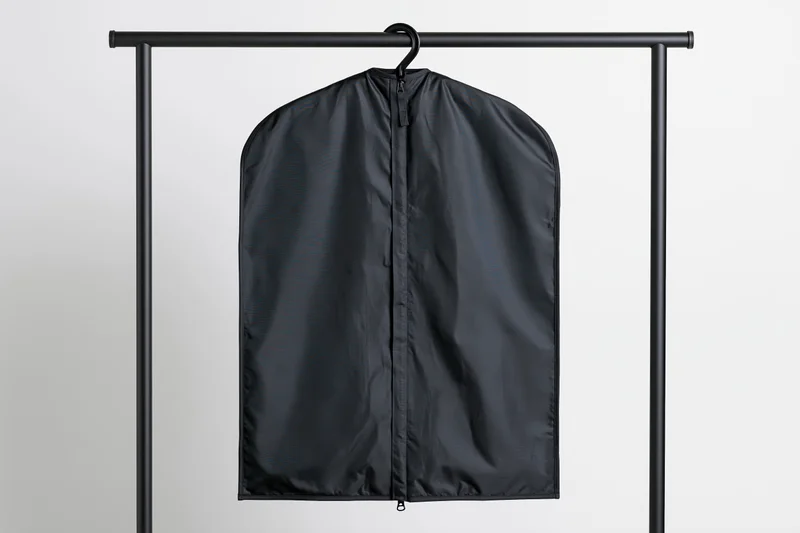 Black garment bag hanging on a metal rack against a plain background