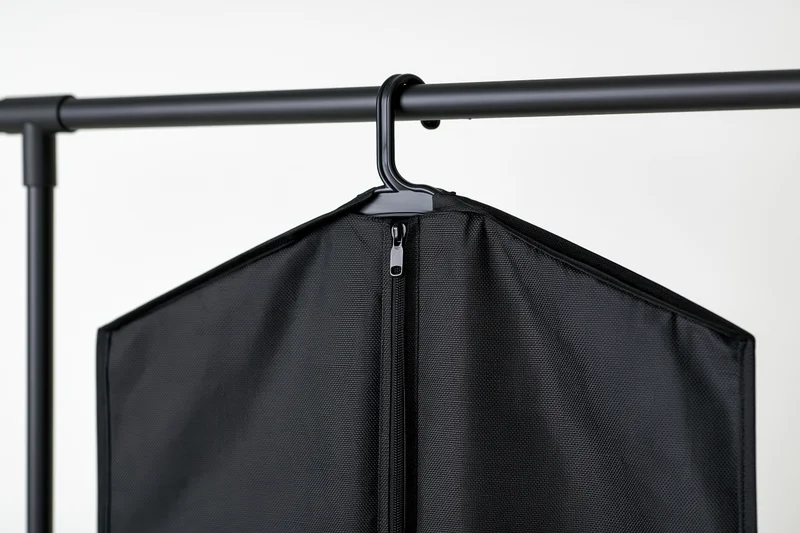 Black fabric garment bag hanging on matte black metal rack against white background