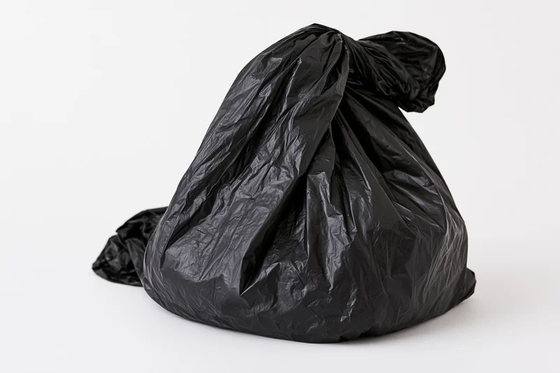 Black plastic garbage bag tied and crumpled on white background